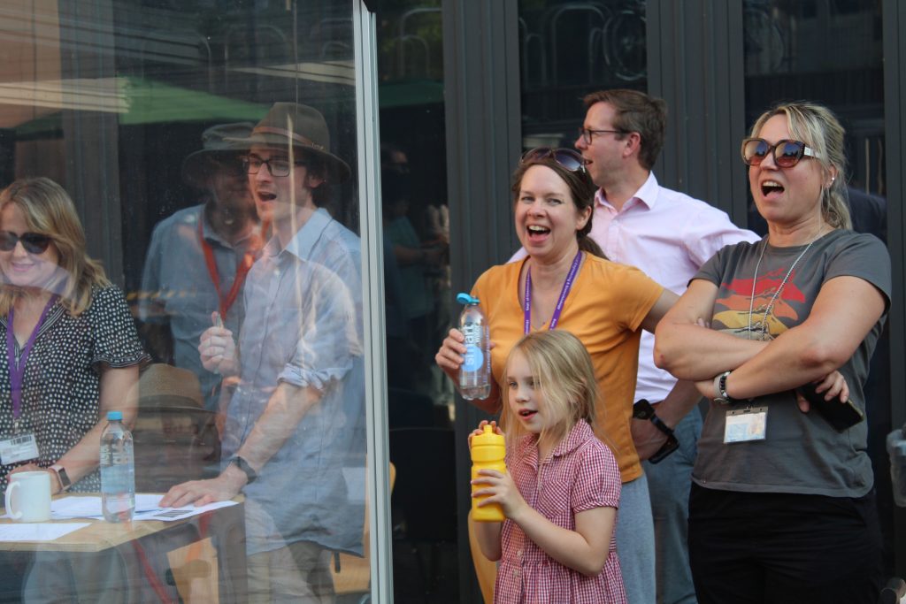 People smile and cheeer at something off camera, in a relaxed setting.