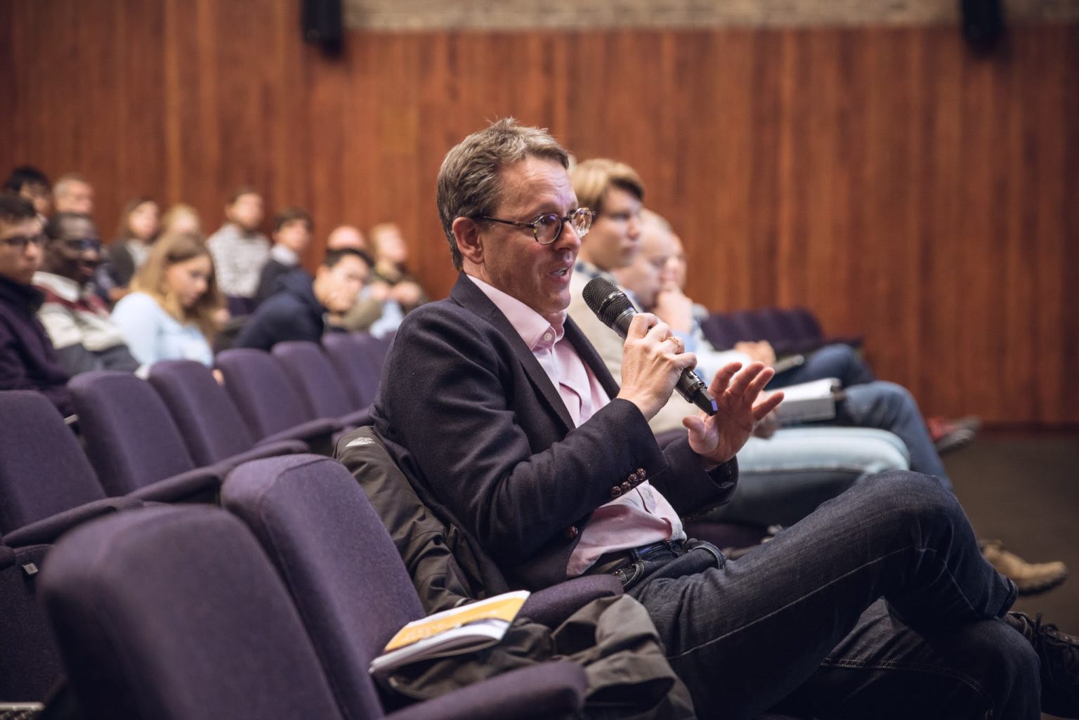 Prof Clemens Kaminski in a lecture theatre seating with a microphone asking a question of someone off camera.